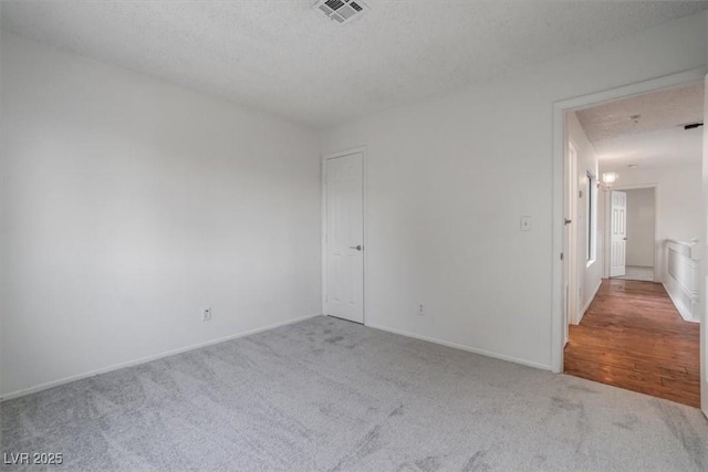 spare room featuring light colored carpet and a textured ceiling