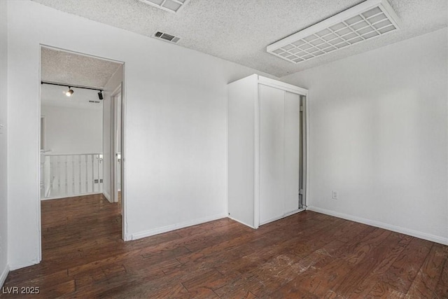 unfurnished bedroom with a closet, dark hardwood / wood-style floors, a textured ceiling, and rail lighting