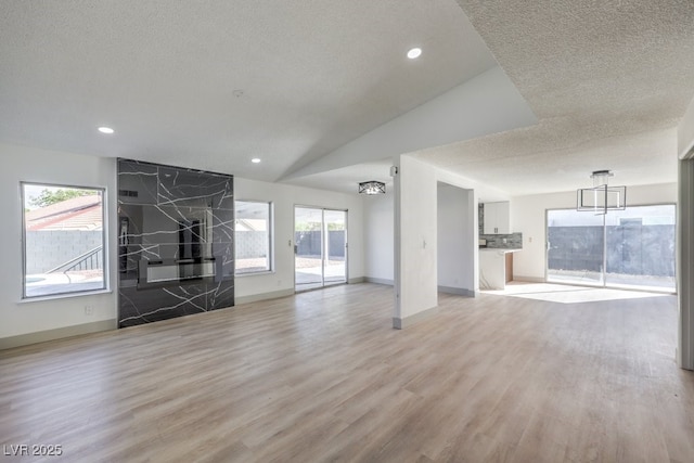 unfurnished living room featuring vaulted ceiling, a textured ceiling, and light hardwood / wood-style flooring