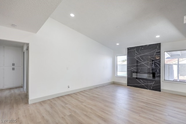 spare room featuring lofted ceiling, light hardwood / wood-style flooring, and a textured ceiling