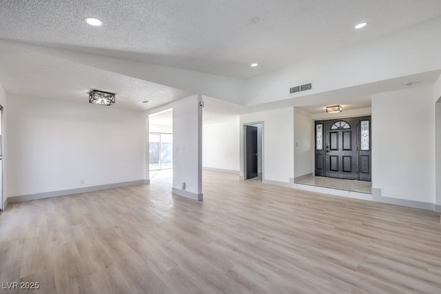 unfurnished living room with lofted ceiling, a textured ceiling, and light wood-type flooring