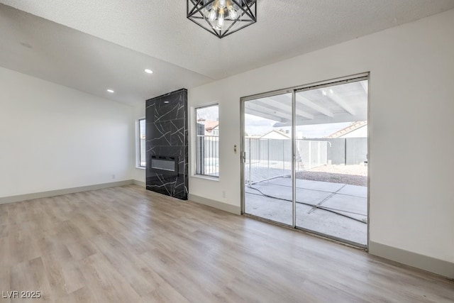 unfurnished living room featuring a high end fireplace, a chandelier, a textured ceiling, and light wood-type flooring