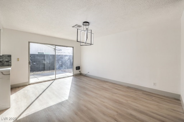 unfurnished dining area with light hardwood / wood-style floors, a chandelier, and a textured ceiling