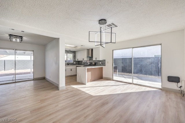 kitchen featuring sink, white cabinets, hanging light fixtures, light wood-type flooring, and wall chimney exhaust hood