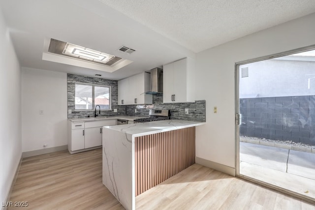 kitchen with stainless steel stove, white cabinets, light hardwood / wood-style floors, kitchen peninsula, and wall chimney exhaust hood