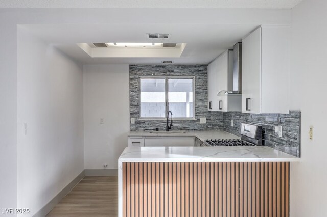 kitchen with wall chimney exhaust hood, sink, stainless steel range, a raised ceiling, and white cabinets