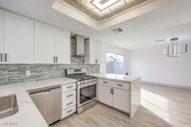 kitchen featuring stainless steel appliances, pendant lighting, wall chimney range hood, and white cabinets