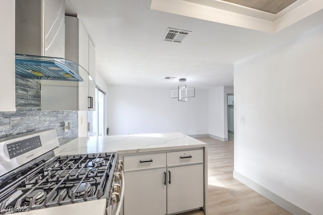 kitchen with wall chimney range hood, tasteful backsplash, white cabinets, stainless steel range with gas cooktop, and kitchen peninsula