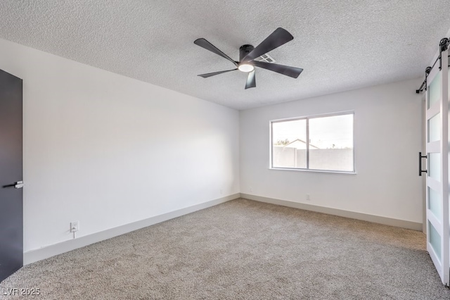 spare room with a textured ceiling, a barn door, ceiling fan, and carpet flooring