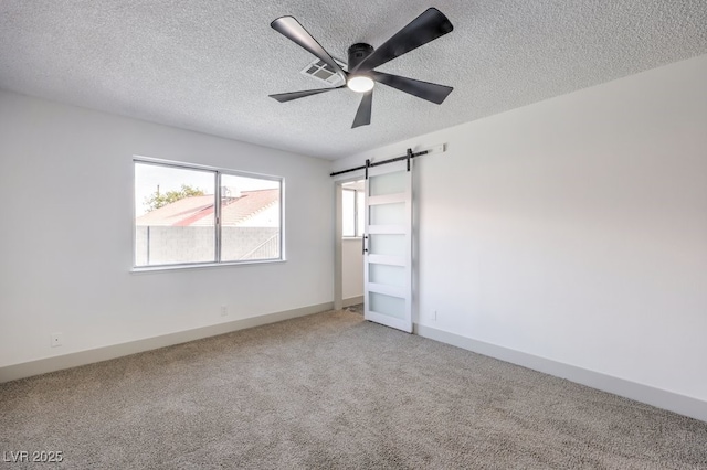 spare room featuring a barn door, carpet flooring, a textured ceiling, and ceiling fan