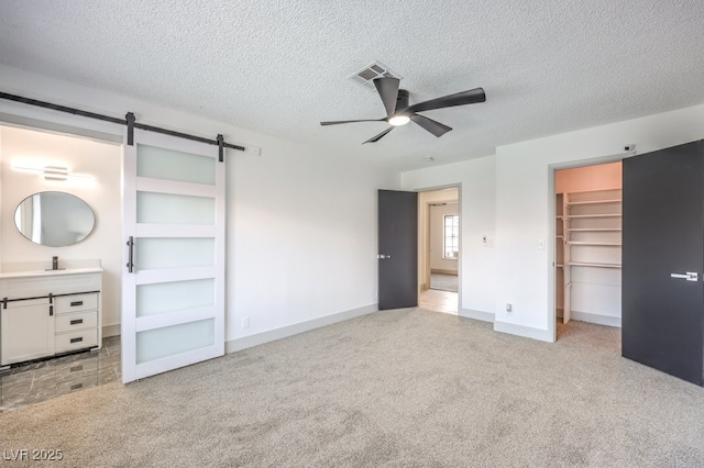 unfurnished bedroom with a barn door, a walk in closet, light carpet, and ceiling fan