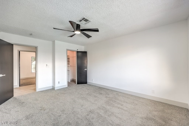 unfurnished bedroom with ceiling fan, a textured ceiling, a walk in closet, light colored carpet, and a closet