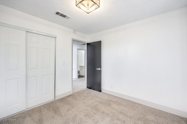 unfurnished bedroom with light colored carpet, a closet, and a textured ceiling