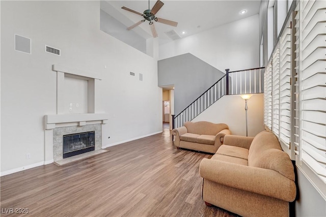 living room with hardwood / wood-style floors, a tile fireplace, ceiling fan, and a high ceiling