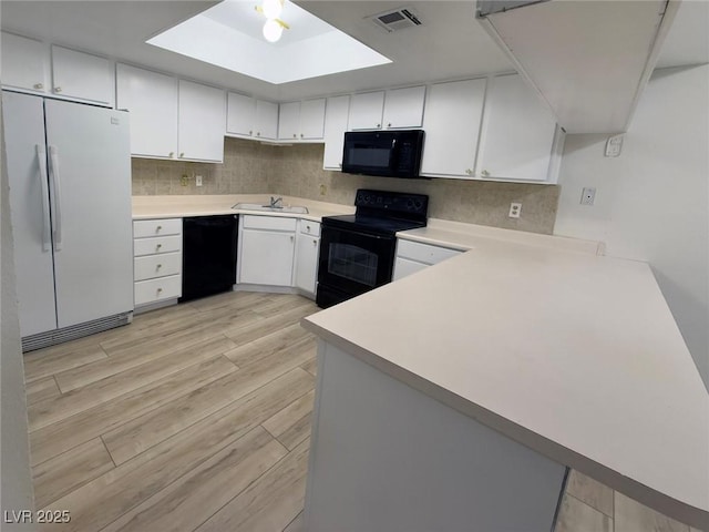 kitchen with white cabinetry, kitchen peninsula, sink, and black appliances