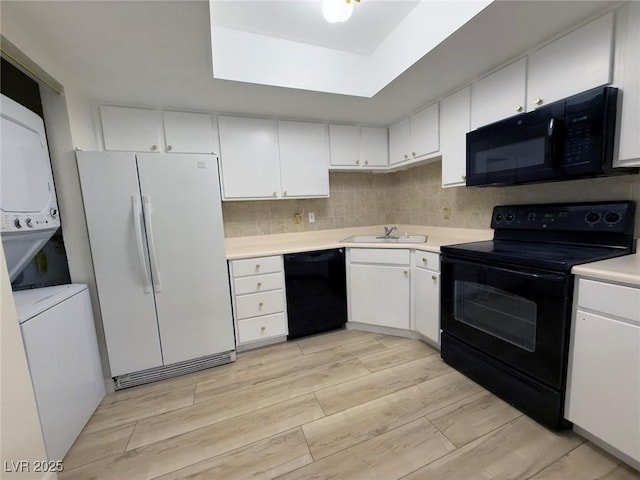 kitchen featuring sink, black appliances, stacked washer / dryer, light hardwood / wood-style floors, and white cabinets