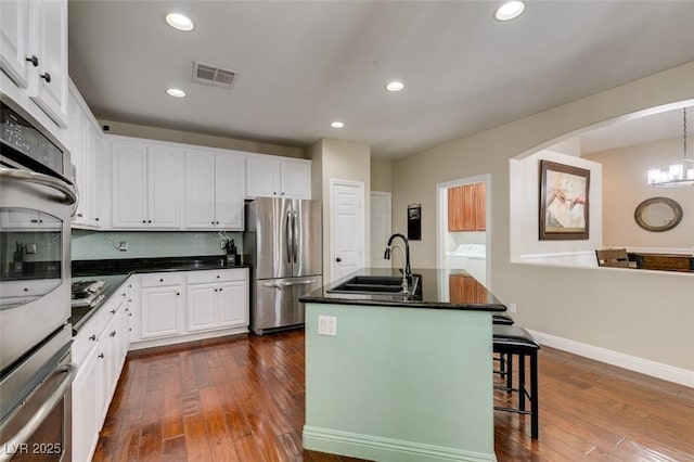 kitchen with an island with sink, white cabinetry, sink, decorative backsplash, and stainless steel appliances