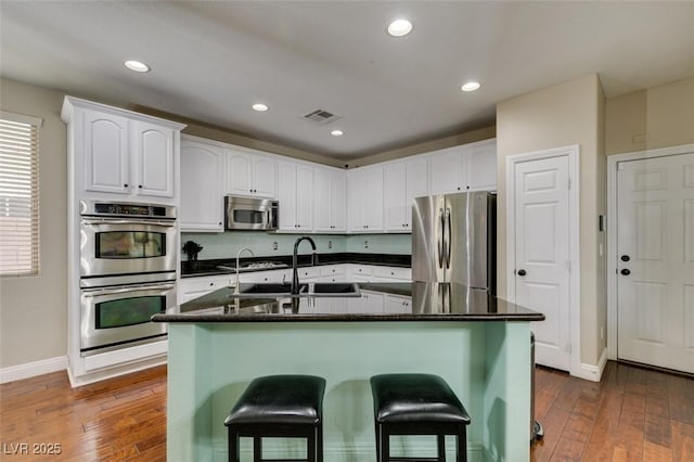 kitchen with sink, dark wood-type flooring, a kitchen island with sink, stainless steel appliances, and white cabinets