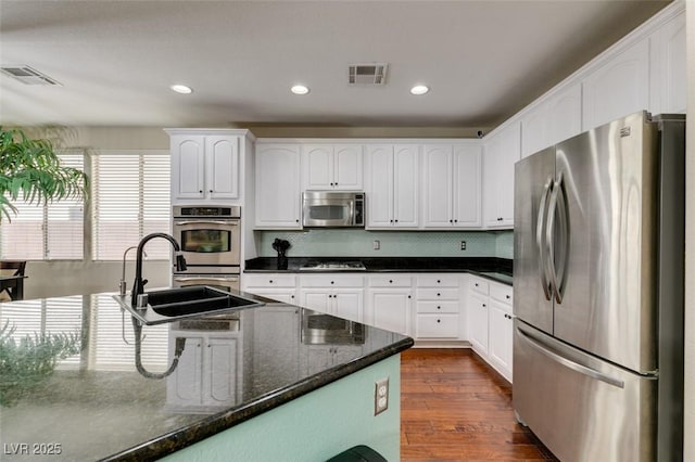 kitchen with white cabinetry, appliances with stainless steel finishes, dark hardwood / wood-style flooring, dark stone counters, and backsplash