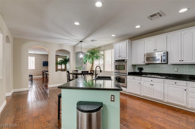 kitchen with appliances with stainless steel finishes, pendant lighting, white cabinetry, sink, and a kitchen island with sink