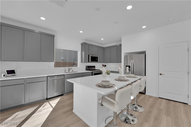 kitchen with light wood-type flooring, stainless steel appliances, gray cabinets, and a kitchen island