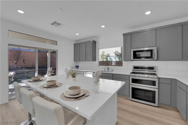 kitchen with light hardwood / wood-style floors, gray cabinets, stainless steel appliances, and a center island