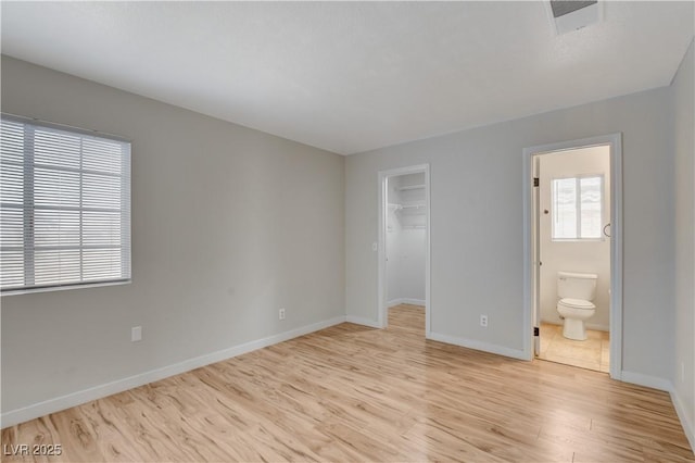 unfurnished bedroom featuring connected bathroom, a walk in closet, a closet, and light wood-type flooring