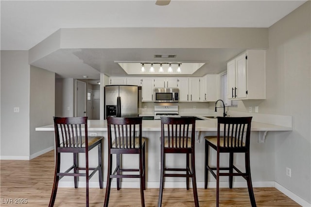 kitchen featuring appliances with stainless steel finishes, white cabinets, a kitchen bar, and kitchen peninsula