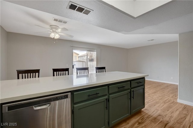 kitchen featuring a textured ceiling, stainless steel dishwasher, green cabinets, ceiling fan, and light hardwood / wood-style floors