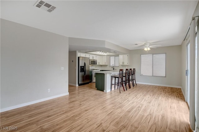 kitchen featuring a breakfast bar, appliances with stainless steel finishes, kitchen peninsula, light hardwood / wood-style floors, and white cabinets