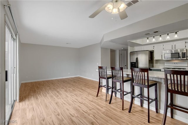 kitchen featuring a breakfast bar, light hardwood / wood-style flooring, ceiling fan, stainless steel appliances, and white cabinets