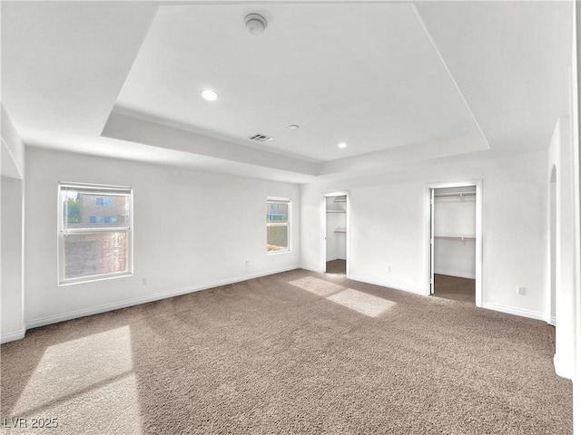 unfurnished bedroom featuring a tray ceiling, a spacious closet, carpet, and a closet