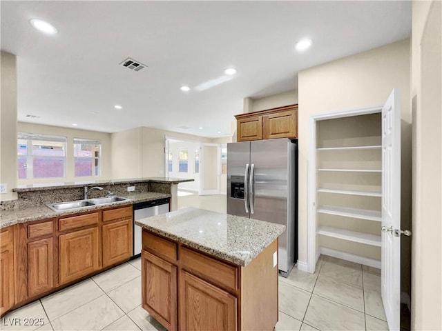 kitchen with sink, appliances with stainless steel finishes, light stone counters, a kitchen island, and light tile patterned flooring