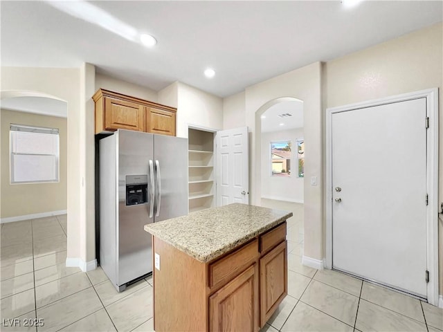 kitchen featuring stainless steel refrigerator with ice dispenser, light stone counters, a kitchen island, and light tile patterned floors