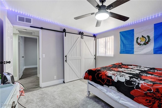 bedroom with a barn door, light colored carpet, a ceiling fan, visible vents, and baseboards