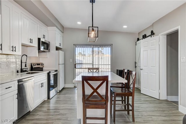 kitchen with a barn door, appliances with stainless steel finishes, decorative light fixtures, white cabinetry, and a sink