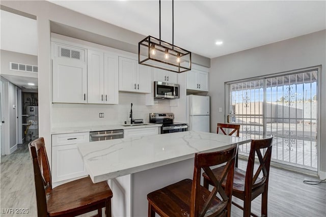 kitchen featuring appliances with stainless steel finishes, white cabinets, visible vents, and hanging light fixtures