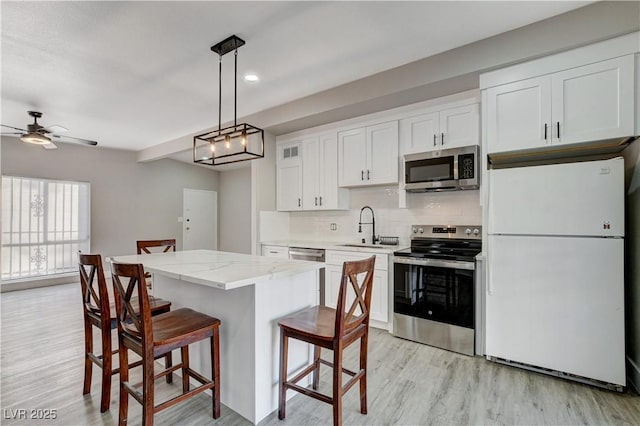 kitchen featuring a breakfast bar, a sink, a kitchen island, white cabinets, and appliances with stainless steel finishes