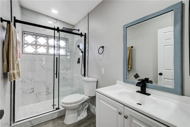 bathroom featuring toilet, a marble finish shower, wood finished floors, and vanity