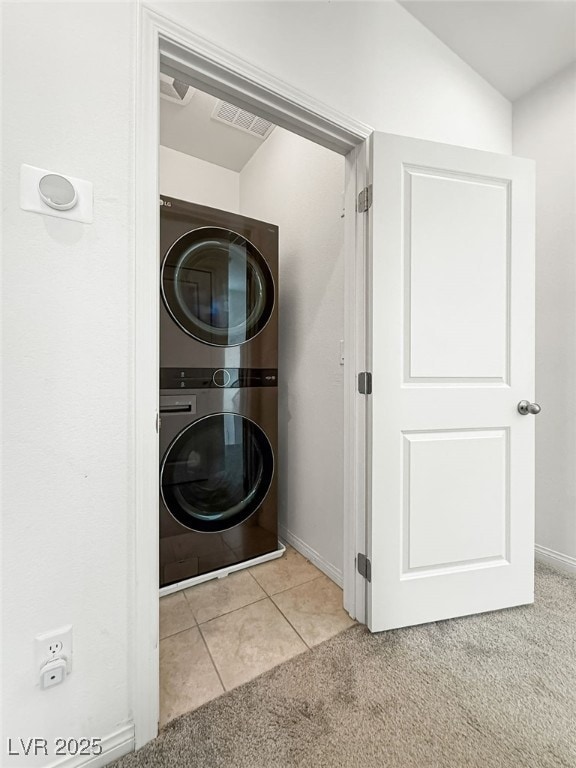 clothes washing area featuring light tile patterned flooring and stacked washing maching and dryer