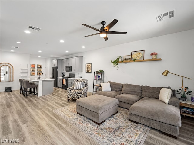 living room featuring sink, ceiling fan, and light hardwood / wood-style flooring