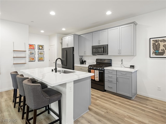 kitchen with stainless steel appliances, an island with sink, sink, and gray cabinetry