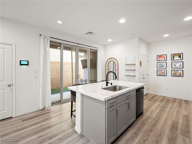 kitchen with sink, gray cabinetry, a center island with sink, stainless steel dishwasher, and light hardwood / wood-style floors