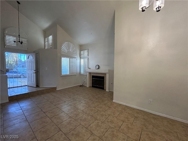 unfurnished living room with baseboards, a fireplace, high vaulted ceiling, and a notable chandelier