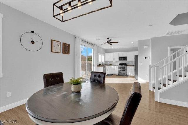 dining room with ceiling fan with notable chandelier and light hardwood / wood-style floors