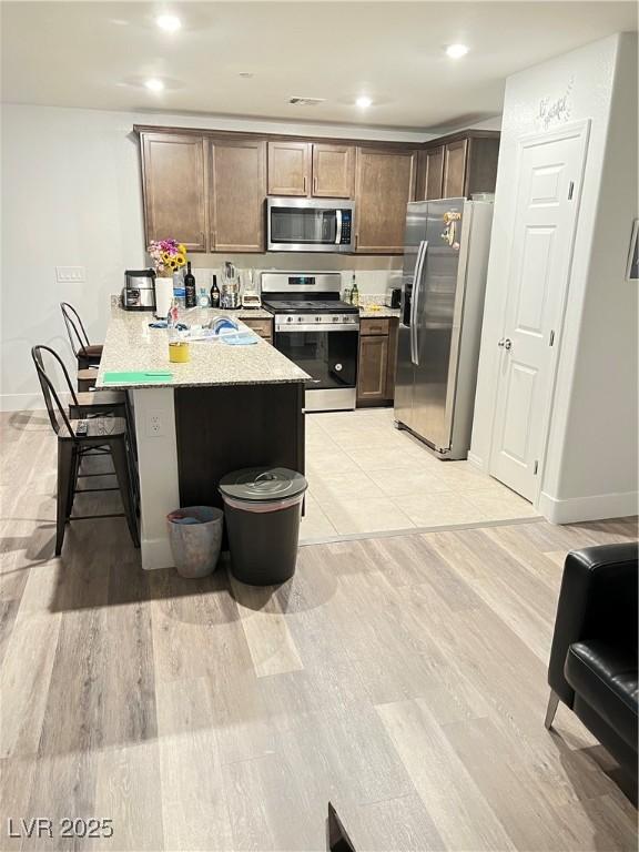 kitchen with a kitchen bar, light hardwood / wood-style flooring, kitchen peninsula, and appliances with stainless steel finishes