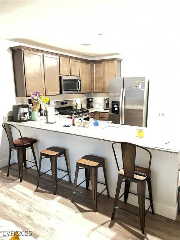 kitchen with light hardwood / wood-style floors, a kitchen breakfast bar, kitchen peninsula, and appliances with stainless steel finishes