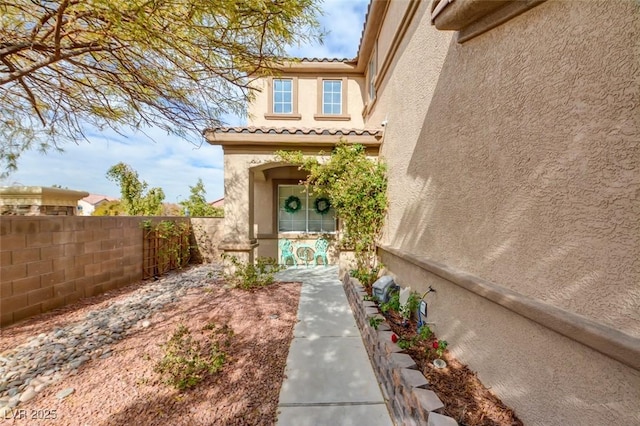 doorway to property featuring fence, a tiled roof, and stucco siding