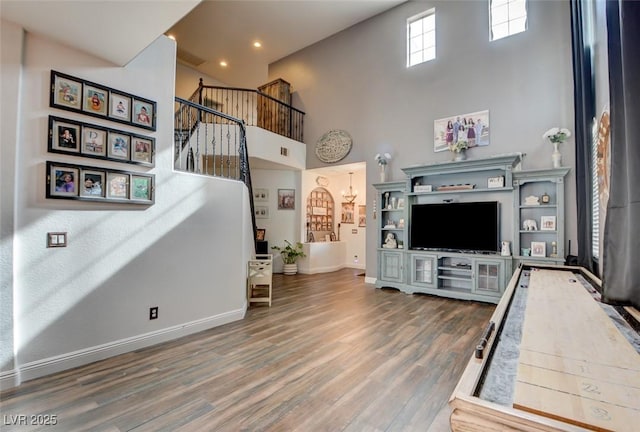 living area with stairs, a towering ceiling, baseboards, and wood finished floors