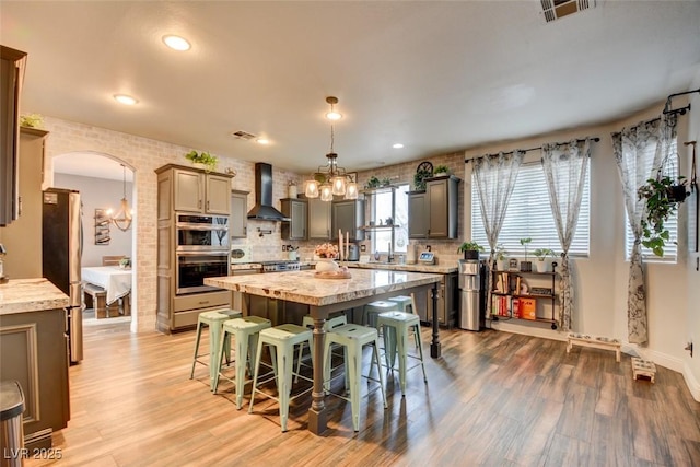 kitchen with a breakfast bar, hanging light fixtures, a center island, stainless steel appliances, and wall chimney exhaust hood